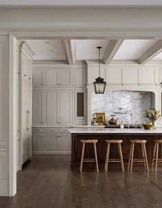 a large kitchen with white cabinets and wood flooring is pictured in this image, there are stools at the center of the island