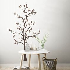 a white table topped with a vase filled with flowers next to a small tree on top of a hard wood floor