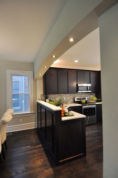 an open kitchen and dining room with wood flooring, white counter tops and black cabinets