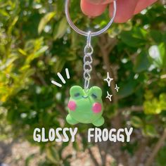 a hand holding a keychain with a frog on it that says glossy froggy