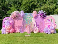 a pink backdrop with balloons and flowers in the shape of butterfly's wings on grass