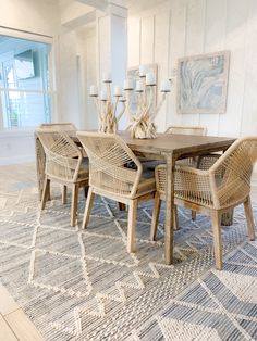 a dining room table and chairs in front of a large window with an area rug on the floor