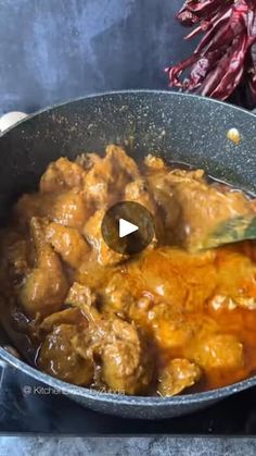 a pan filled with meat and sauce on top of a stove next to red peppers