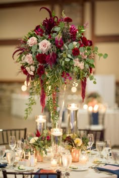 a tall vase filled with lots of flowers on top of a white table cloth covered table