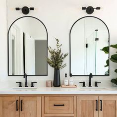 a bathroom with double sinks and mirrors on the wall next to plants in vases