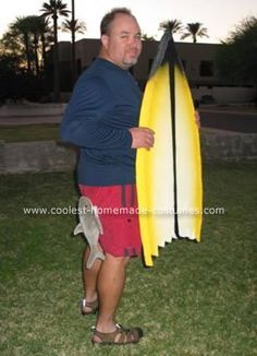 a man holding a yellow surfboard in his right hand while standing on the grass