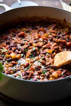 a pot full of beans and vegetables with a wooden spoon