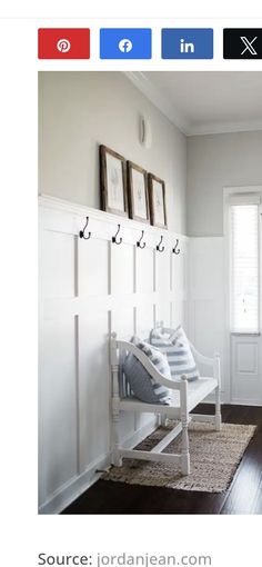 a white bench sitting in the middle of a living room next to a door with hooks on it