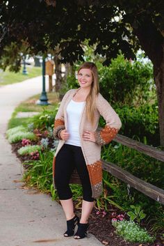 a woman standing on a sidewalk wearing black pants and a cardigan sweater with brown accents