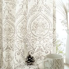 a cup and saucer sitting on a table next to a window with white curtains