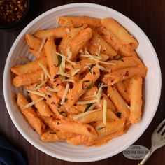 a white bowl filled with pasta and cheese on top of a table next to a fork