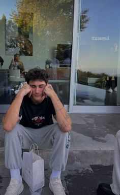 a man sitting on the sidewalk with his hands to his face and looking at something in front of him