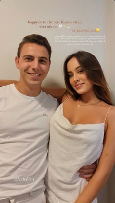 a man standing next to a woman in white clothing and smiling at the camera with her arm around him