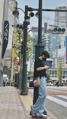 a man standing on the side of a street next to a pole with a cell phone in his hand