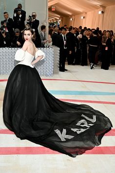 a woman in a black and white gown standing on a red carpet with photographers behind her