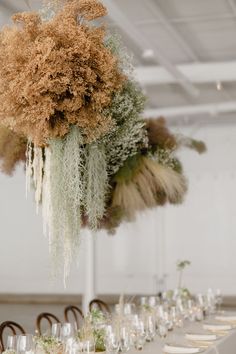 an arrangement of flowers and greenery is suspended from the ceiling over a long table