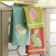 three colorful towels hanging on a rack in front of a table with plates and utensils