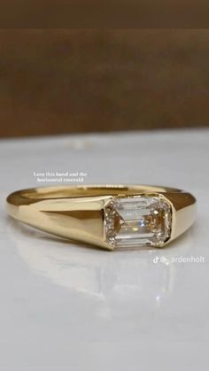 a yellow gold ring with an emerald cut diamond in the center on a white surface