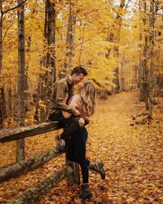 a man and woman standing on a fence in the woods with leaves all around them