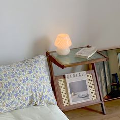 a small table with a lamp on top of it next to a bed and pillows