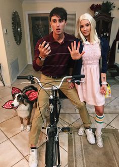 a man and woman sitting on a bicycle with a dog standing next to them, posing for the camera