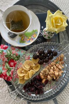 a glass plate topped with fruit and nuts next to a cup of tea