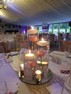 candles are lit in glass vases with flowers on the table at a wedding reception