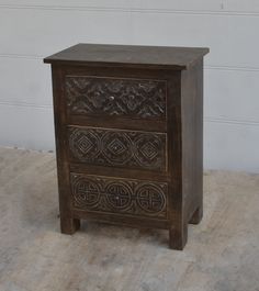 a wooden cabinet with carvings on the front and sides, against a white brick wall