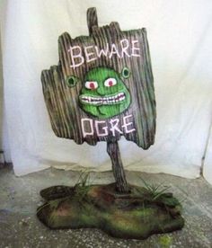 a wooden sign that says beware of the ogre with an evil face on it