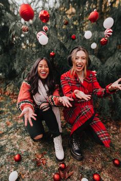 two women sitting on the ground in front of a christmas tree with red and white ornaments