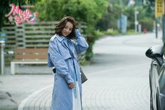 a woman standing next to a parked car on the side of a road with her hand in her hair