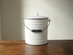 a white bucket sitting on top of a wooden table with a black handle and lid