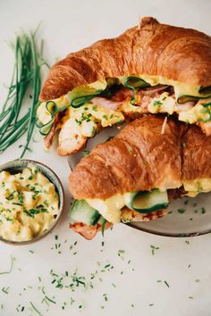 a croissant sandwich cut in half on a plate next to a bowl of dip