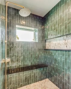 a green tiled bathroom with a window above the shower head and bench in front of it