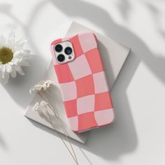 an iphone case sitting on top of a white surface next to a flower and a daisy