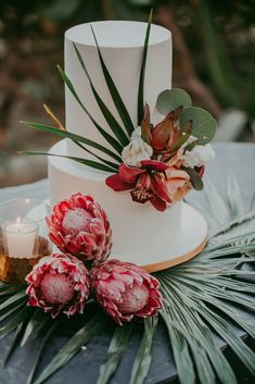 a white wedding cake with red flowers and greenery next to it on a table