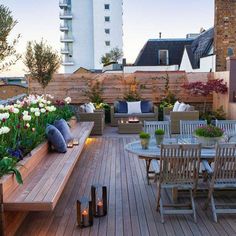 a wooden deck with chairs and table surrounded by flowers, plants and candles on it