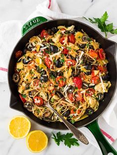 a skillet filled with pasta, olives, tomatoes and parmesan cheese