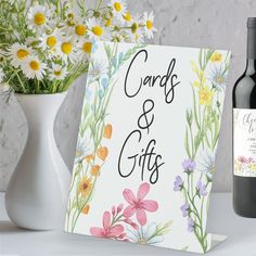 a bottle of wine next to a card and vase with flowers