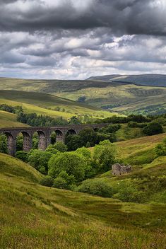 an old train traveling over a lush green hillside under a cloudy sky with mountains in the background