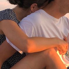 a man and woman sitting next to each other on a boat in the water at sunset