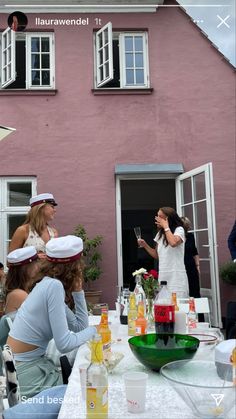 a group of people sitting around a table with plates and cups in front of a pink house