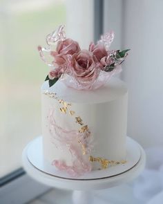 a white cake with pink flowers and gold leaf decorations on it's top tier