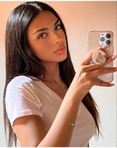 a woman taking a selfie with her cell phone in front of her and wearing a white t - shirt