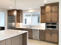 an empty kitchen with stainless steel appliances and wood cabinets, along with white counter tops