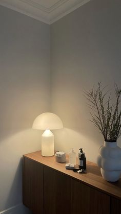 a white vase sitting on top of a wooden table next to a lamp and other items