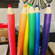 several colored pencils are sitting in front of each other on a table next to a fan