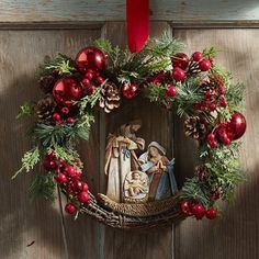 a nativity wreath hanging on a door with red balls and pine cones around it