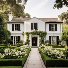 a large white house surrounded by hedges and flowers