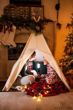 two people sitting in a teepee with christmas stockings on the floor next to a fire place